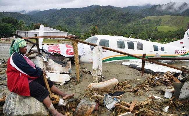 Warga duduk di dekat pesawat yang terseret banjir bandang di Sentani, Jaya Pura, Papua, Senin (18/3/2019). (Foto :  ANTARA/Zabur Karuru)