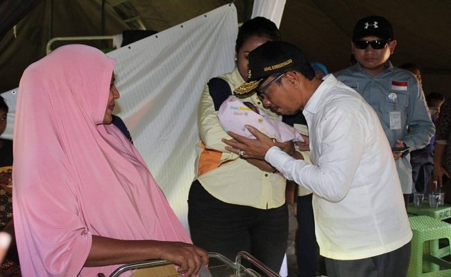Wakil Gubernur Maluku Barnabas Orno, mencium bayi Muhammad Abas Orno Pelu saat ditimang Ibu Baetrix Orno, di tenda pengungsian, kawasan Kampus Unidar Ambon, Tulehu, Kecamatan Salahutu, Selasa (1/10/2019) (FOTO: HUMASMALUKU) 